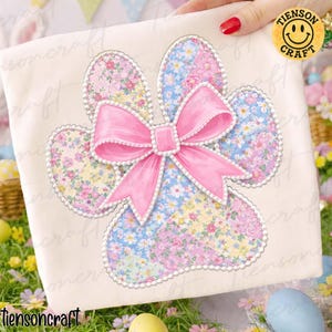 May include: A cream-coloured fabric featuring a floral bunny paw print design. The paw print is made of patchwork fabric in pastel colours and a pink bow. The design is outlined with a white beaded trim. The text "tiensoncraft" is at the bottom.