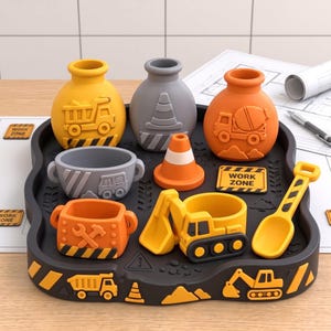 May include: A black construction-themed tray holding various containers and accessories. Items include a yellow dump truck vase, a gray traffic cone vase, an orange cement mixer vase, a gray bowl, an orange cone, a yellow excavator, and a yellow shovel.