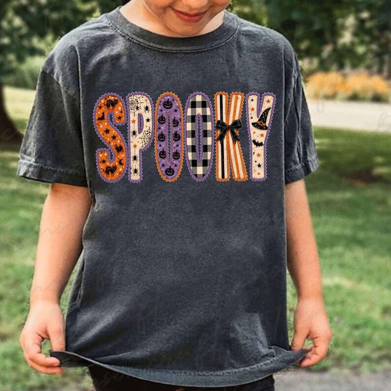 Może przedstawiać: Ciemnoszary t-shirt z kr&oacute;tkim rękawem z napisem SPOOKY na piersi. Każda litera ma unikalny wz&oacute;r, w tym pomarańczowe dynie, pajęczyny, fioletowe dynie, czarno-białą kratę oraz kapelusz czarownicy.