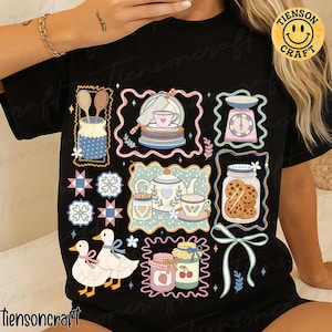 以下が含まれることがあります： キッチンをテーマにしたデザインの黒いTシャツ。デザインには、キッチン用品、ティーカップ、クッキー、アヒルのイラストが含まれています。「tiensoncraft」の文字がTシャツの下部にプリントされています。黄色のスマイリーフェイスのロゴが右上にあります。