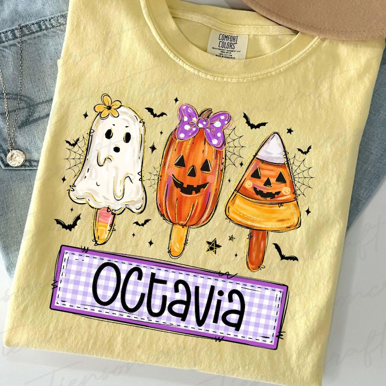 Peut inclure: T-shirt jaune avec un motif d'Halloween. Le graphisme pr&eacute;sente trois personnages en forme de sucettes glac&eacute;es : un fant&ocirc;me, une citrouille et un bonbon. Le nom "Octavia" est dans un encadr&eacute; &agrave; carreaux violets et blancs. Des chauves-souris et des toiles d'araign&eacute;es noires sont &eacute;galement incluses.