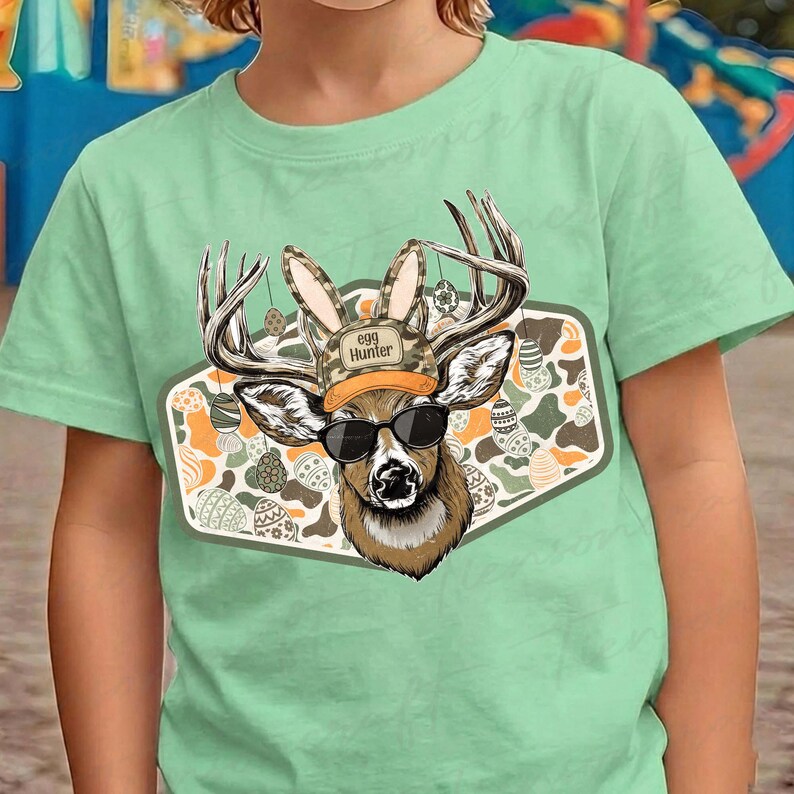 May include: A light green t-shirt featuring a graphic of a deer wearing sunglasses, a camouflage hat with the text "Egg Hunter", and bunny ears. The deer is set against a patterned background with Easter eggs.