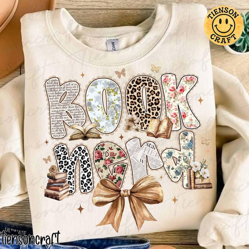 Puede incluir: Sudadera crema con las palabras "BOOK NERD" en un dise&ntilde;o decorativo. Las letras presentan patrones florales, de leopardo y tem&aacute;ticos de libros. Un gran lazo marr&oacute;n y mariposas completan el dise&ntilde;o.