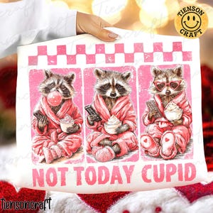 May include: A white pillowcase featuring three raccoons in pink robes, each holding a remote and a cup of whipped cream. One raccoon blows a bubble. The text "NOT TODAY CUPID" is printed below the raccoons.