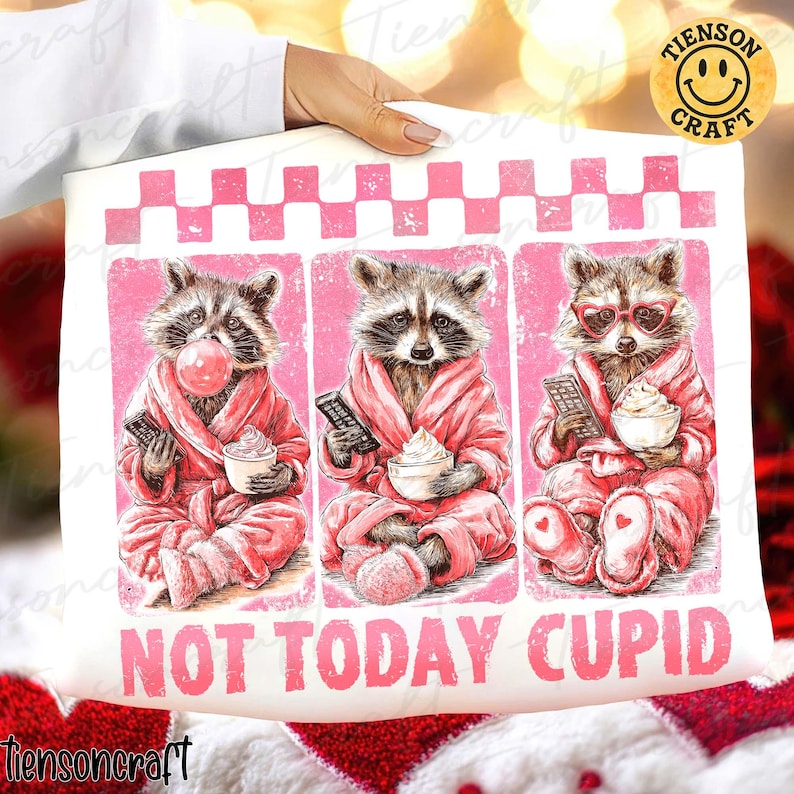 May include: A white pillowcase featuring three raccoons in pink robes, each holding a remote and a cup of whipped cream. One raccoon blows a bubble. The text "NOT TODAY CUPID" is printed below the raccoons.