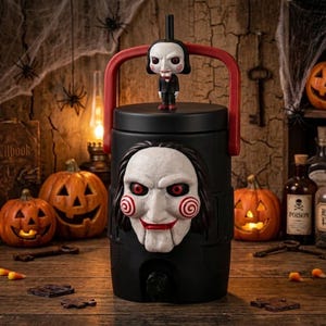 May include: A black beverage dispenser featuring a sculpted Billy the Puppet face on the front, a red carrying handle, and a small Billy the Puppet figure attached to the top lid. The dispenser has a black spigot at the base for pouring.