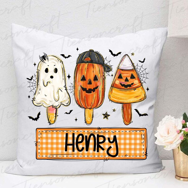 Peut inclure: Coussin blanc avec un motif sur le th&egrave;me d'Halloween. Il pr&eacute;sente trois personnages en forme de sucettes glac&eacute;es : un fant&ocirc;me, une citrouille portant une casquette et un bonbon en forme d'&eacute;pi de ma&iuml;s. Le nom "HENRY" est affich&eacute; sur une banni&egrave;re &agrave; carreaux en dessous.
