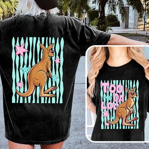 May include: Black t-shirt with a kangaroo wearing sunglasses, set against a teal and black striped background with pink and blue stars. The text "TOO DA LOO" is also visible.