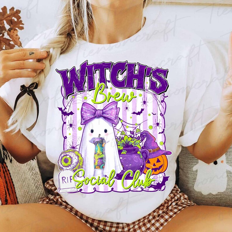 May include: White t-shirt with a Halloween-themed graphic. The design features a ghost with a purple bow, a cauldron, a jack-o'-lantern, and the text "Witch's Brew Social Club" in purple and green. Spiders and bats are also included.