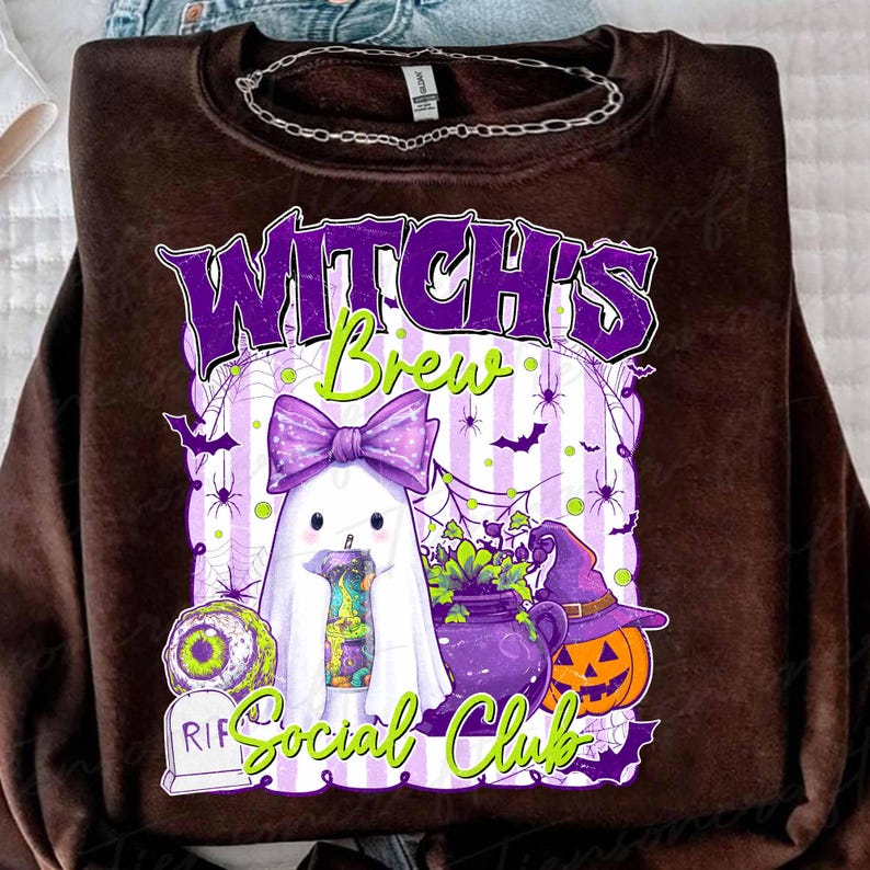 May include: Brown sweatshirt with a Halloween-themed graphic. The design features a ghost with a purple bow, a cauldron, a jack-o'-lantern, and the text "Witch's Brew Social Club" in purple and green. Spiders and bats are also included.