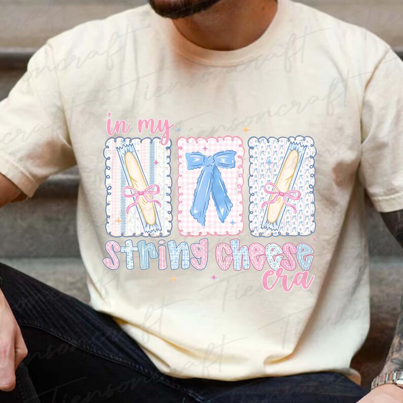 May include: Cream-colored t-shirt with a graphic design featuring the text "in my string cheese cra." The design includes three rectangular frames with string cheese and bows in pink and blue.