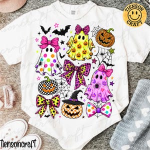 May include: A white t-shirt featuring a colorful Halloween-themed graphic print. The design includes three ghosts wearing bows, three jack-o'-lanterns with various patterns, spider webs, bats, stars, and several decorative bows in bright colors.