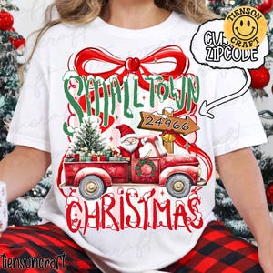 May include: White t-shirt with a Christmas-themed design. The graphic shows a red pickup truck laden with a Christmas tree and presents, with Santa Claus at the wheel. The words "Small Town Christmas" are displayed in a festive font, with the postcode 24966.