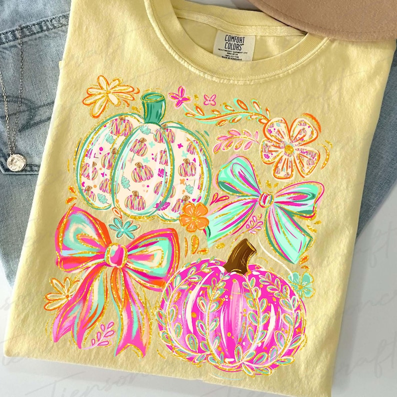 May include: A yellow Comfort Colors t-shirt featuring a colorful fall design. The design includes pumpkins, bows, and floral elements in shades of pink, teal, orange, and gold. The shirt is laid flat on a surface.