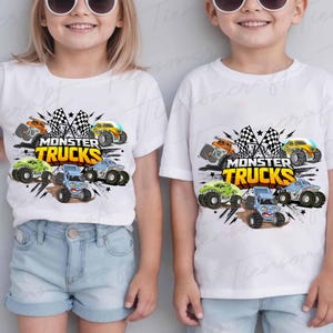 May include: White t-shirts featuring a vibrant graphic of monster trucks. The design showcases monster trucks in orange, yellow, green, and blue, accompanied by checkered flags and the text "Monster Trucks" in yellow.