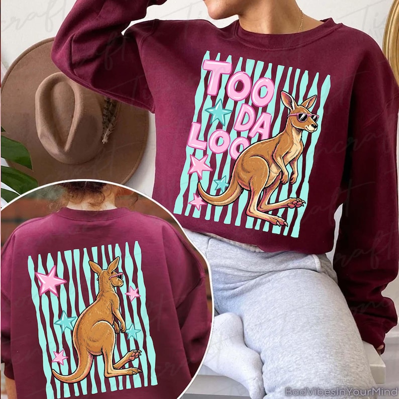 May include: A burgundy sweatshirt with a kangaroo wearing sunglasses and the text "Too Da Loo" in pink. The kangaroo is set against a light blue striped background with pink and blue stars. The back of the sweatshirt also features the kangaroo design.