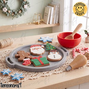 May include: A gray circular tray holding wooden Christmas-themed shapes including a Santa Claus, a gingerbread person, a snowman, a green gift box, a red stocking, and a Christmas tree. A red bowl with a wooden spoon and candy canes are nearby.