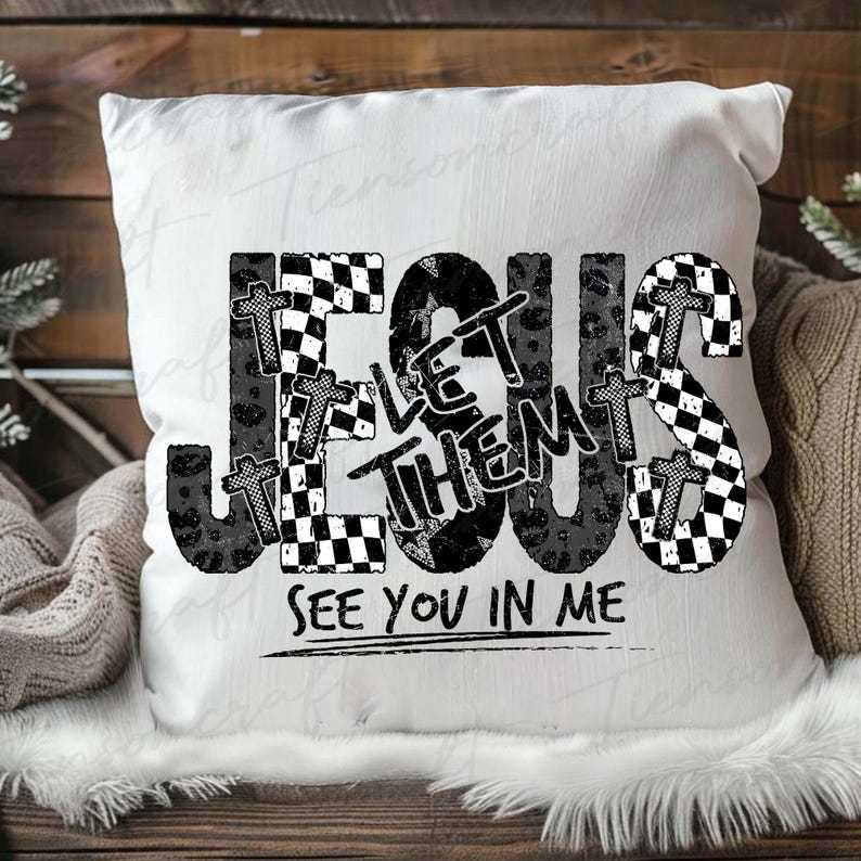 May include: White square cushion with the words "JESUS LET THEM SEE YOU IN ME" in black, with checkered and cross designs. The cushion is on a wooden surface.