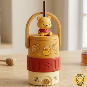 May include: A cylindrical yellow and red beverage container featuring a Winnie the Pooh figure on the lid, a metal straw, and a handle. The body displays honey pot, honeycomb, and bee graphics, with a small spigot at the base for dispensing liquid.