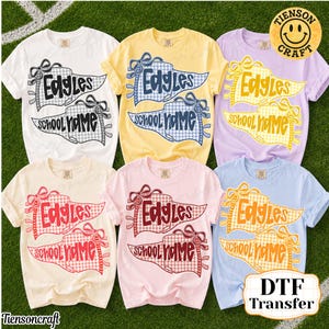 May include: Six short-sleeved t-shirts in white, yellow, lavender, cream, pink, and light blue. Each shirt features a graphic of two pennants with bows, displaying the text "Edgles" and "school name" in a checkered pattern matching the shirt color.