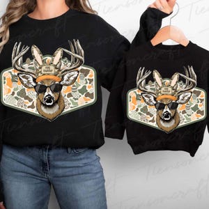 May include: Black sweatshirts with a deer graphic wearing sunglasses and bunny ears. The deer is on a patterned background with Easter eggs. The text "Egg Hunter" is on the deer's hat. One sweatshirt is adult size, the other is child size.