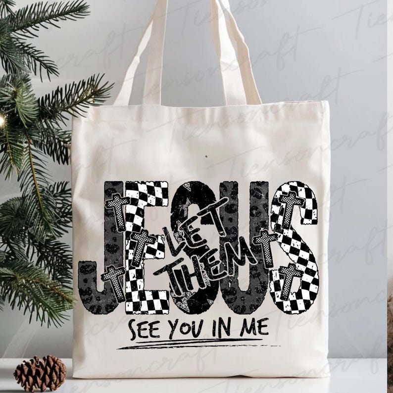 May include: Cream tote bag featuring the text "JESUS LET THEM SEE YOU IN ME" in a black and white checkered and leopard print design. The bag has two handles and is made of a canvas-like material.