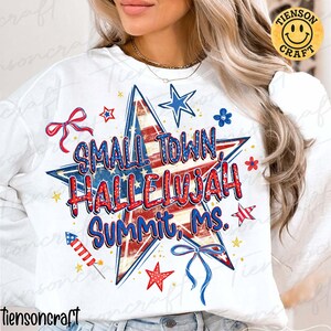 Puede incluir: Una sudadera blanca de manga larga con una gran estrella central con un patrón de bandera roja, blanca y azul. El texto "SMALL TOWN, HALLELUJAH SUMMIT, MS." está rodeado de pequeñas estrellas rojas y azules, fuegos artificiales y lazos azules.
