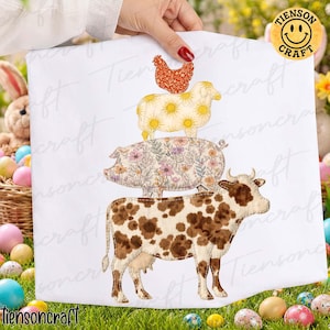 May include: A white fabric featuring a stack of farm animals: a brown and white cow, a pig with floral patterns, a sheep with yellow sun designs, and a red chicken. The design is held by a hand.