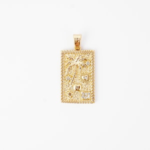 Puede incluir: Colgante rectangular dorado con un diseño de palmera, pequeñas piedras transparentes y un borde texturizado. El colgante tiene una argolla en la parte superior para una cadena. El diseño incluye una palmera, estrellas y otros elementos tropicales.
