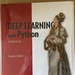 Op de afbeelding: Het boek getiteld Deep Learning with Python Second Edition van François Chollet heeft een rood-witte kaft. De kaft toont een illustratie van een persoon in historische kleding met lange vloeiende stof, uitgegeven door Manning.