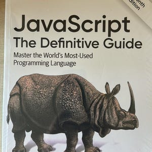 Op de afbeelding: Een wit paperbackboek getiteld JavaScript The Definitive Guide, Seventh Edition, door David Flanagan. De omslag bevat een grote, gedetailleerde illustratie van een bruine neushoorn en het O'Reilly-logo in rode tekst linksboven.
