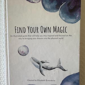 以下が含まれることがあります： 「Find Your Own Magic」というタイトルの本。クジラと月の水彩イラストが描かれています。表紙には「Find Your Own Magic」の文字と、著者Elizabeth Ermenkovaの名前が記載されています。本は透明なプラスチックで包装されています。