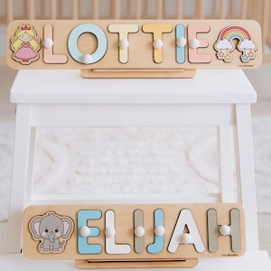 Pu&ograve; includere: Due puzzle di nomi in legno per bambini, con i nomi "Lottie" ed "Elijah". Il puzzle "Lottie" presenta una principessa e un arcobaleno, mentre il puzzle "Elijah" ha un elefante. Ogni puzzle ha lettere colorate e pioli.