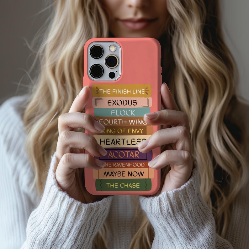 Pu&ograve; includere: Custodia per telefono color corallo con una pila di dorsi di libri colorati. I dorsi mostrano titoli come "THE FINISH LINE", "EXODUS" e "FLOCK". La custodia &egrave; tenuta da una persona con un maglione bianco.