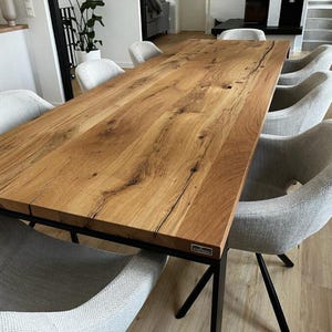 Könnte beinhalten: Ein großer, rechteckiger Esstisch aus Holz mit natürlicher Holzmaserung. Der Tisch ist von sechs grau gepolsterten Stühlen mit schwarzen Metallbeinen umgeben. Der Tisch ist etwa 244 cm lang.