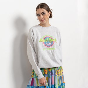 May include: A light gray crewneck sweatshirt featuring a Hard Rock Cafe St. Thomas logo in neon green and pink, paired with a multi-colored tiered mini skirt with floral and striped patterns, and metallic silver knee-high boots.