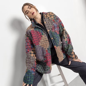 Puede incluir: Chaqueta acolchada de patchwork con varios estampados de cuadros, incluyendo rojo, verde y marrón. La chaqueta tiene una botonadura frontal y un cuello. La modelo lleva una camisa negra y pantalones azul oscuro.