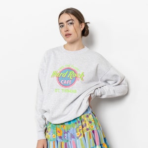 May include: A light gray crewneck sweatshirt featuring a Hard Rock Cafe St. Thomas logo with neon green and pink text. Paired with a tiered mini skirt displaying a vibrant patchwork pattern of blue, yellow, and pink floral and striped prints.