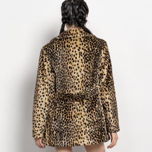 May include: A faux fur coat with a leopard print pattern. The coat features a notched collar, long sleeves, and a matching belt. The coat's colors include tan, brown, and black.