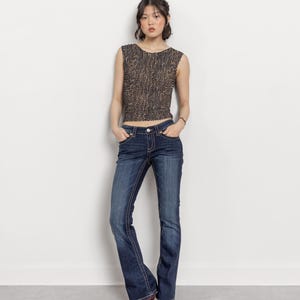 May include: A sleeveless, textured top in shades of brown and black paired with dark wash blue jeans. The jeans have a slight flare at the bottom. The outfit is completed with burgundy heels.