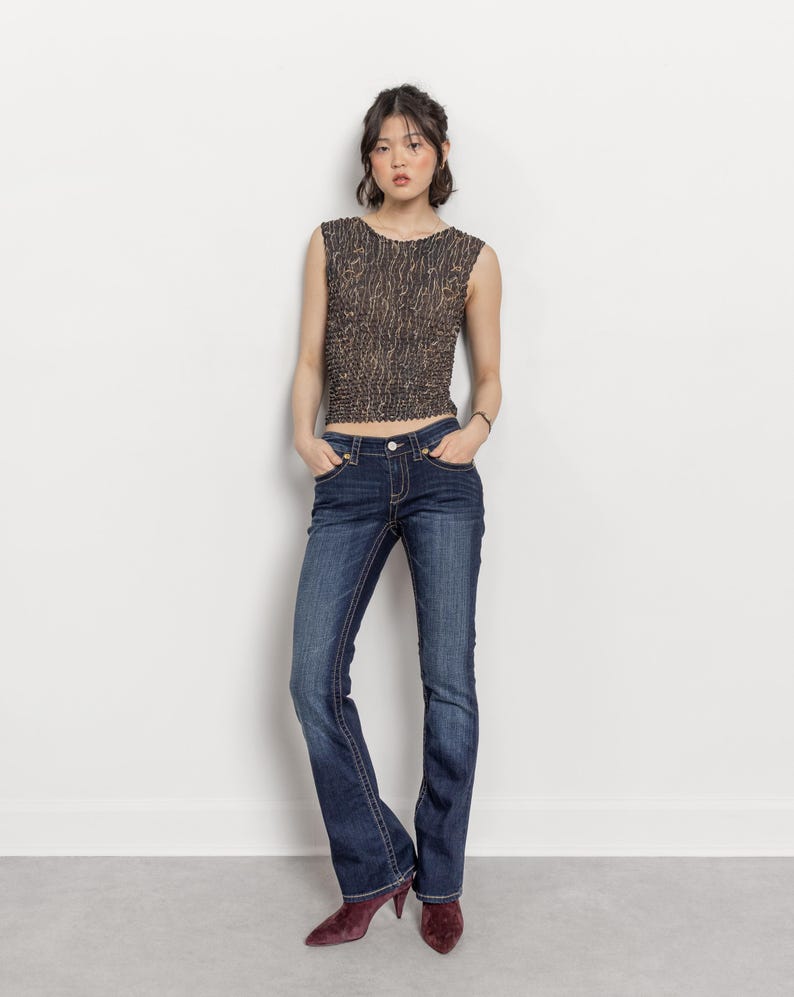May include: A sleeveless, textured top in shades of brown and black paired with dark wash blue jeans. The jeans have a slight flare at the bottom. The outfit is completed with burgundy heels.
