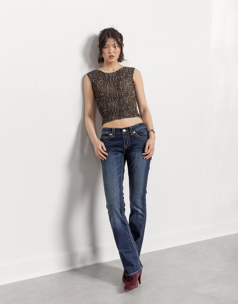 May include: A sleeveless, cropped top with a brown and black pattern is paired with dark wash blue jeans. The jeans have a slight flare at the bottom and are worn with burgundy heels. The outfit is casual and stylish.