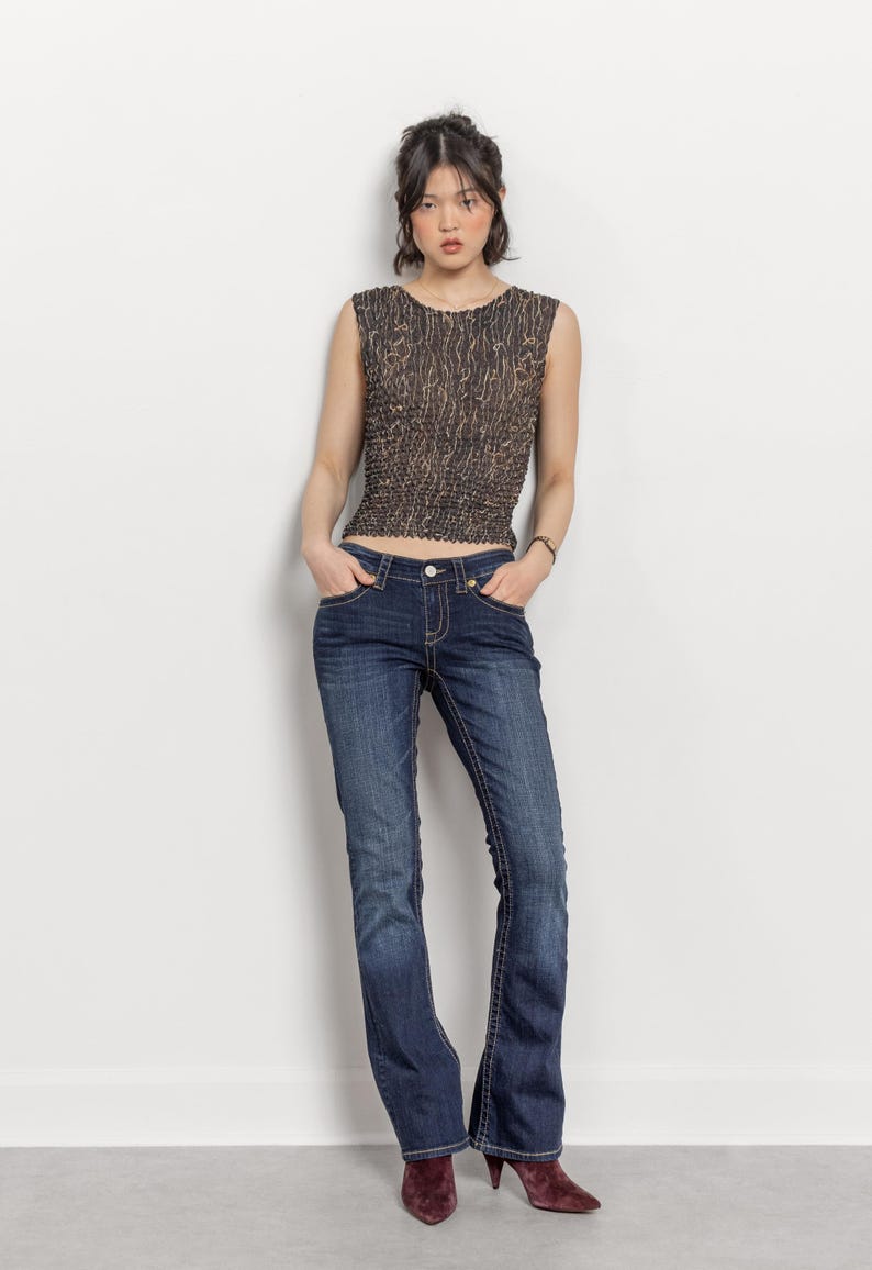 May include: A sleeveless, brown and tan patterned top paired with dark wash blue jeans. The jeans have a slight flare at the bottom. The model is wearing burgundy heels.