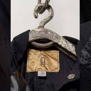 Puede incluir: Chaqueta negra con una etiqueta marr&oacute;n en el bolsillo que dice "DRIZA-BONE". La chaqueta tiene una etiqueta en el interior que dice "DRIZA-BONE RIDING DONE". La chaqueta tiene un bolsillo con el texto "DRIZA-BONE CARE".