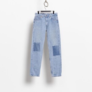 May include: Light blue denim jeans featuring a high-waisted cut, a classic five-pocket design, and a button fly closure. The legs of the jeans are accented with rectangular dark blue denim patches positioned over each knee area.