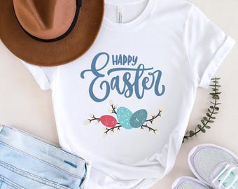 May include: White t-shirt with the text "Happy Easter" in blue script and a graphic of three pastel Easter eggs with white branches and flowers.