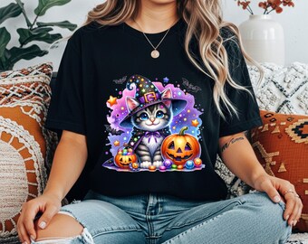 Puede incluir: Camiseta negra con un gato de dibujos animados con sombrero y capa de bruja, junto a una calabaza tallada y decoraciones de Halloween. El gato tiene ojos azules y está rodeado de estrellas y murciélagos. Un diseño divertido para Halloween.