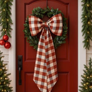 Puede incluir: Una puerta de entrada roja adornada con una corona verde y un gran lazo a cuadros de búfalo en rojo, blanco y gris. La puerta está flanqueada por guirnaldas navideñas y pequeños árboles con luces.