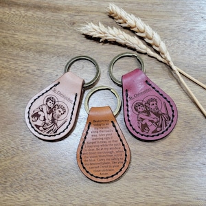 Puede incluir: Tres llaveros de cuero con anillos de metal. Uno es de color canela, otro burdeos y otro marrón. Cada llavero presenta una imagen religiosa de San Cristóbal y un niño. El llavero marrón tiene una oración impresa.