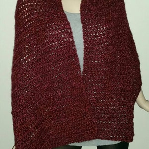 May include: A burgundy crocheted shawl with a lacy pattern. The shawl is draped over a person's shoulders and is worn with a grey shirt and black leggings.